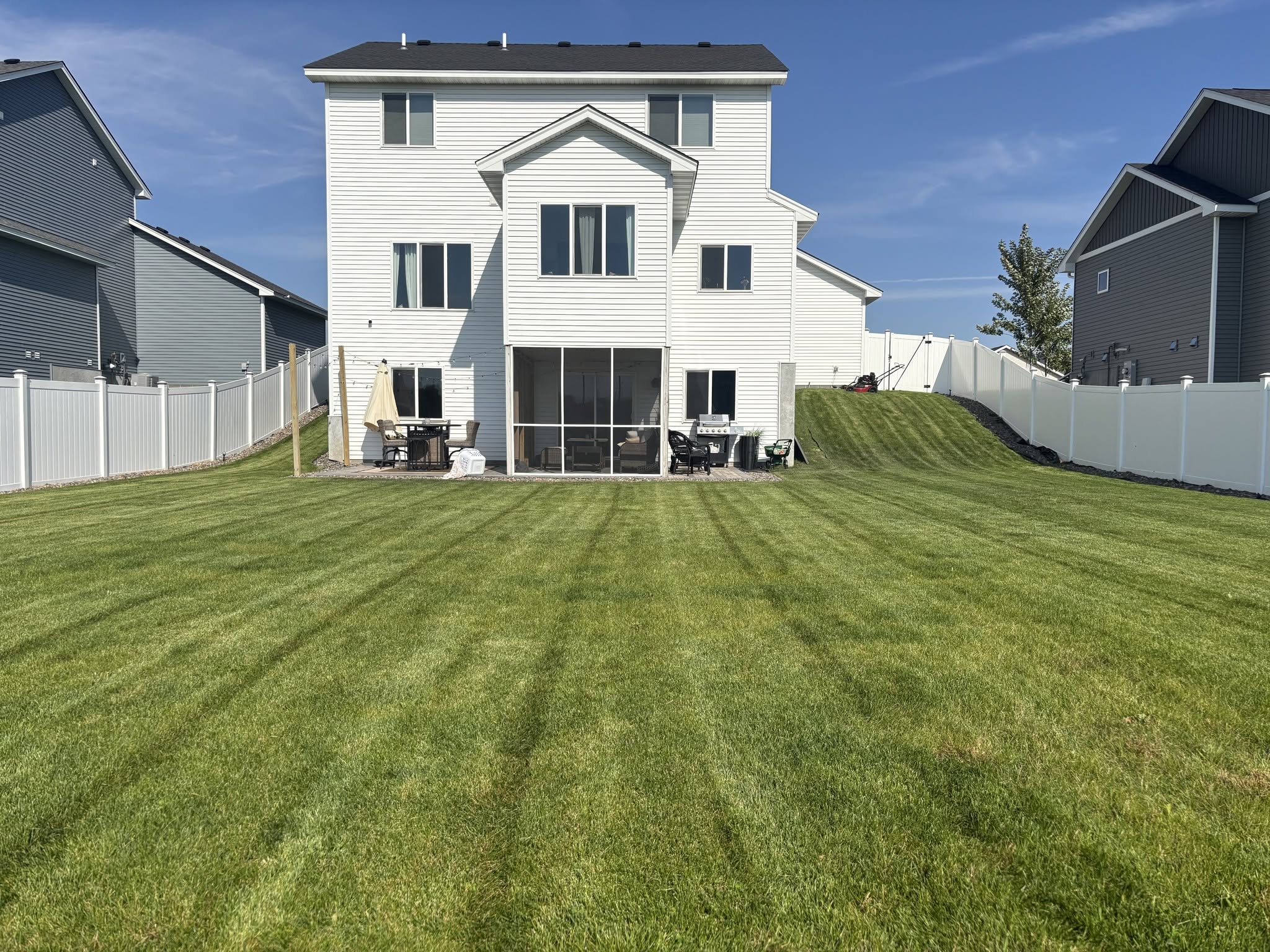 Freshly mowed backyard with lawn stripes beside a white house and fence